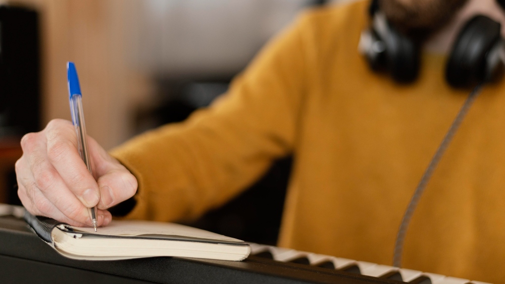 musician at a keyboard taking notes in a notebook